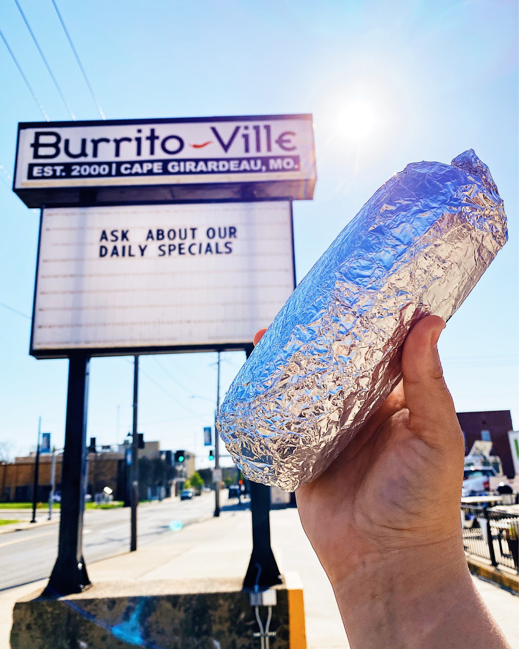 Person holding up a tin foil wrapped burrito in front of the Burrito Ville sign located in Southeast Missouri